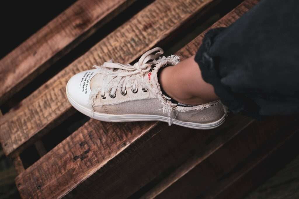 Frayed beige sneaker on wooden pallet evokes rustic urban style.