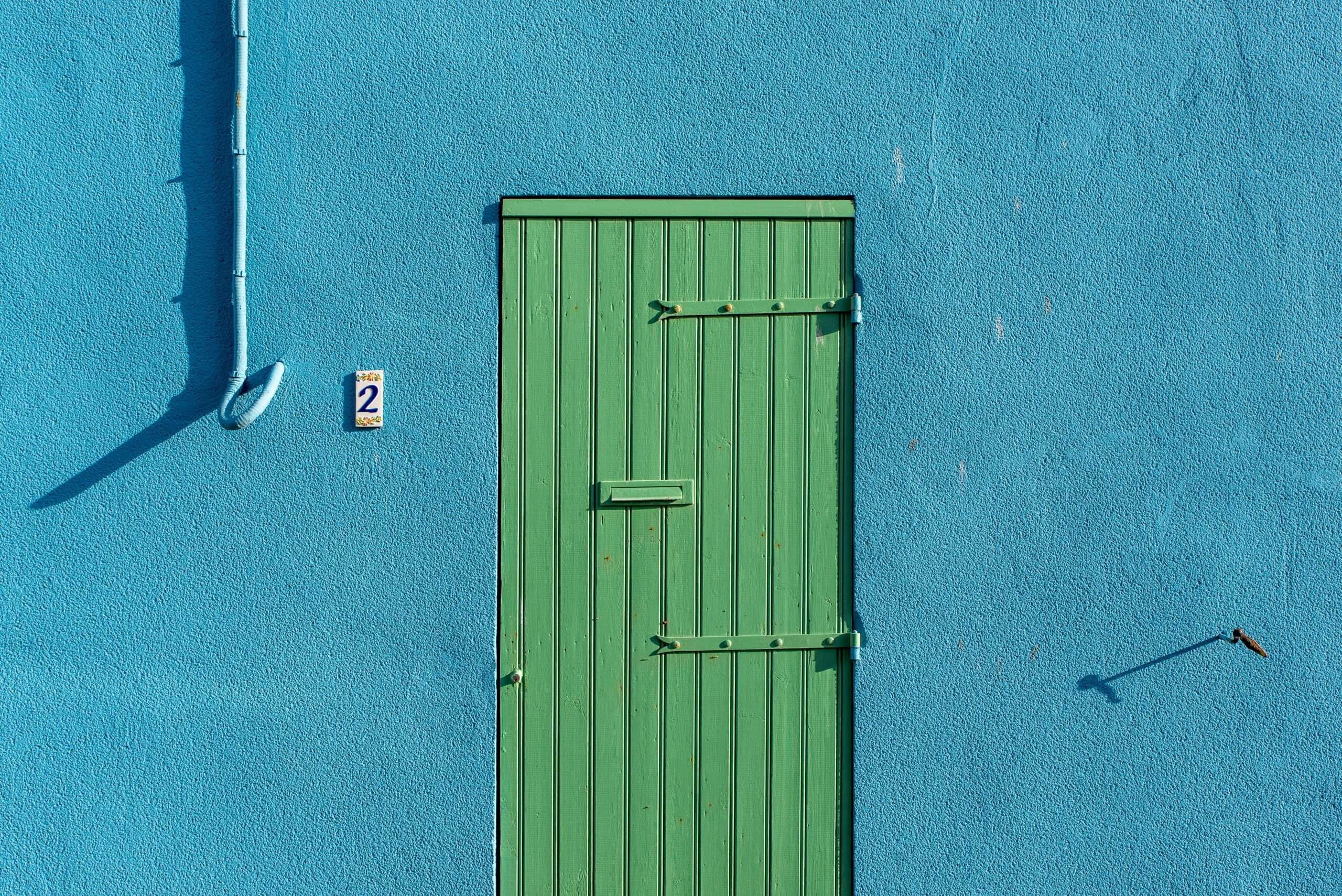 Minimalist image of a green door set against a bright blue wall, creating strong contrast.